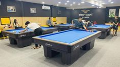 several people are playing pool in an indoor recreation room with blue tables and yellow chairs