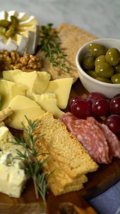 an assortment of cheeses, crackers and olives on a wooden platter