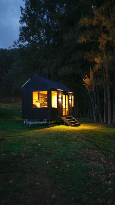 a tiny cabin in the woods at night with lights on and steps leading up to it
