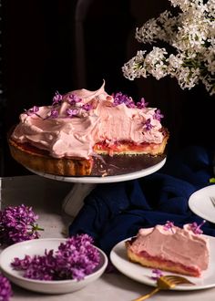 there is a cake with pink frosting on the top and purple flowers in the background