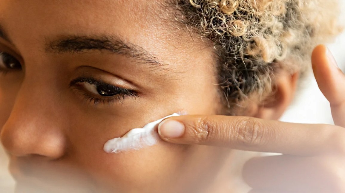 Woman rubbing white cream on her face with one finger.