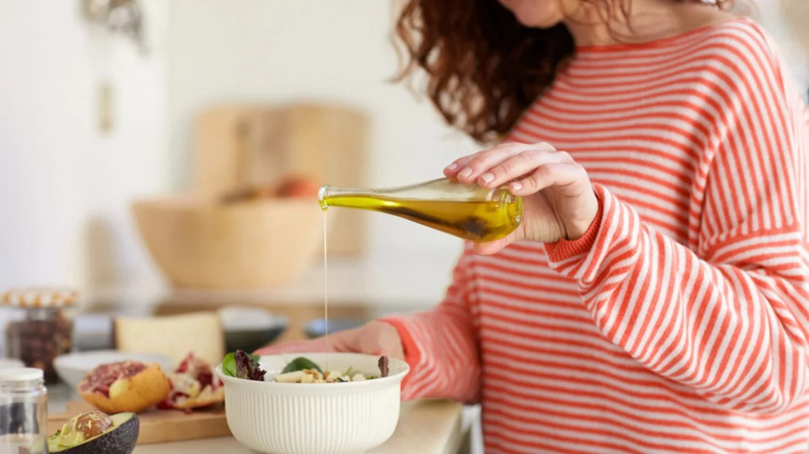 female drizzling olive oil in salad