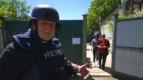 The BBC's Jeremy Bowen standing in front of woman being evacuated from her home