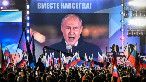Getty Images Vladimir Putin speaks to crowds in Moscow, with the words "Together forever" at the top of the screen.
