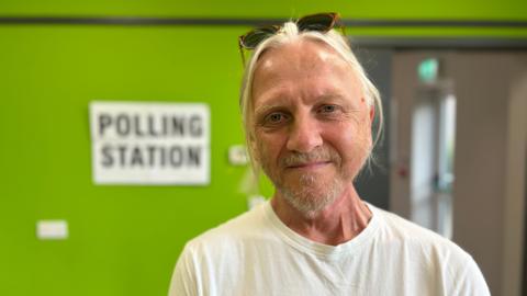 Presiding officer Andy Wragg stands in front of a green wall with a polling station sign displayed