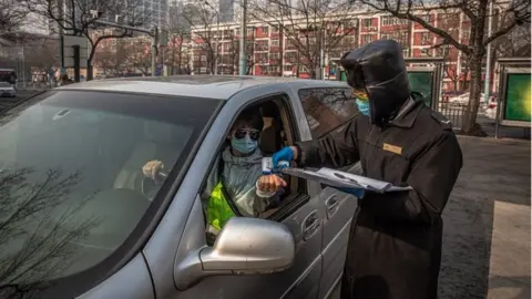 EPA A security guard wearing a protective face mask checks body temperature of a driver at the entrance to a parking at residential area of Sanlitun in Beijing, China, 11 February 2020.