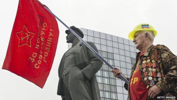 Man with a red flag standing next to a statue of Lenin