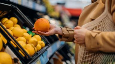 Woman holds orange in supermarket