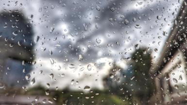 Raindrops in focus on a window pane, with a blurred view of a grey sky beyond