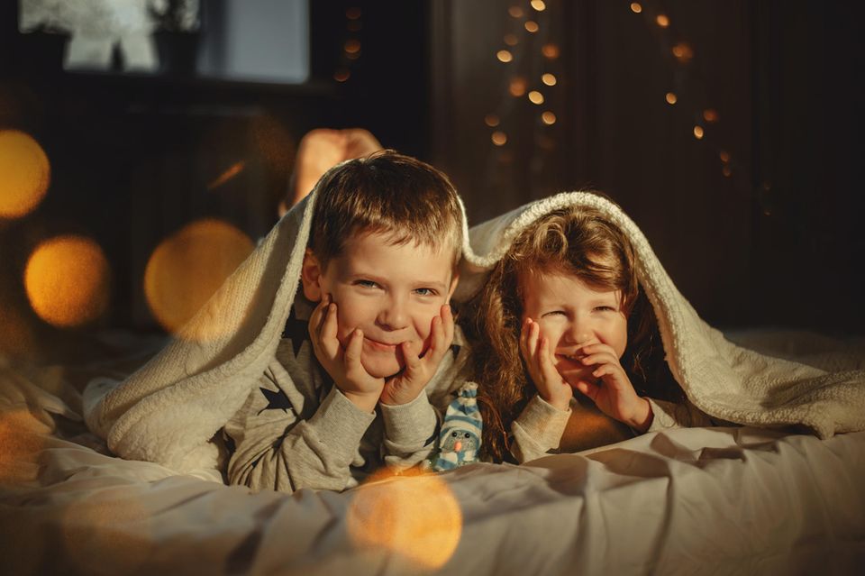 Adventskalender Alternativen: Zwei Kinder liegen morgens gespannt im Bett