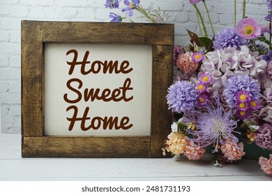 Home sweet home text message motivational and inspiration quote with flowers decoration on white brick wall and wooden background