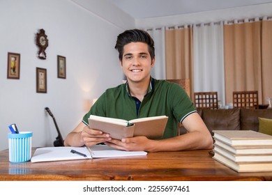 Smiling cute teenage boy studying with books - indoors stock photo. Royalty free image smart boy student teenage boy, sitting on chair, studying with books, at home - smiling face Foto Stock