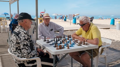 Tres personas juegan al ajedrez a la sombra en la playa de Levante de Benidorm.