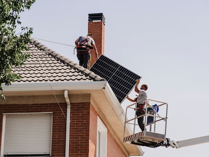 Dos técnicos instalan placas fotovoltaicas en el tejado de una vivienda.