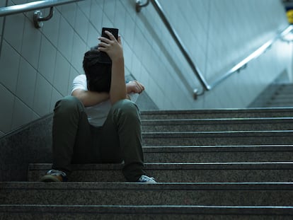 Un adolescente sentado solo llora con un teléfono móvil en la mano, en una imagen de archivo.