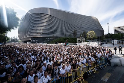 Cientos de personas esperan la llegada de los jugadores con el estadio, al fondo.