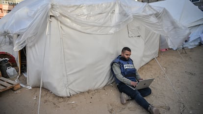 Un periodista sentado junto a una tienda de campaña mientras intenta conectarse a internet en Rafah, Gaza