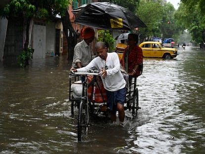Varias personas caminan en un carro por una calle inundada tras la llegada del ciclón Remal el 27 de mayo en Calcuta, India.