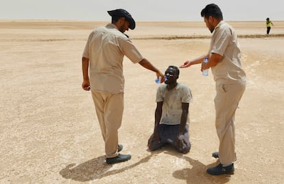 Dos agentes fronterizos libios dan agua a un migrante africano en una zona desértica en la frontera entre Túnez y Libia, en julio de 2023.  