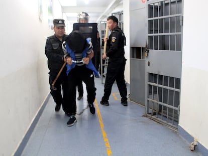 Un recluso de un centro de reeducación del condado de Tekes, en Xinjiang, encapuchado, con esposas y grilletes en los pies, es trasladado por agentes en septiembre de 2018.