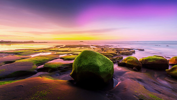 A beautifully edited photo of a rocky landscape, with unusual purple hues on the horizon.