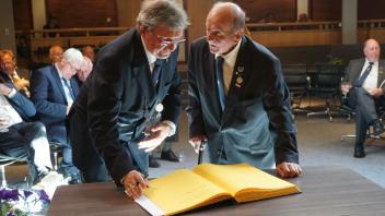 Ehrenältermann Arnold Metzger und Ältermann Hermann Wolter stehen bei dem goldenen Buch der Eckernförder Beliebung.