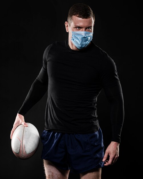 Mężczyzna gracz rugby z medyczną maską trzymając piłkę