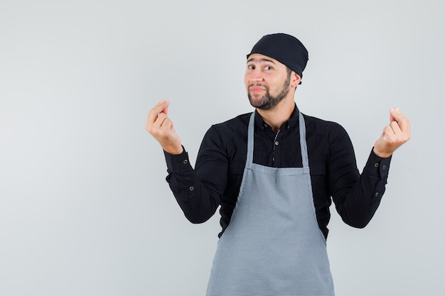 Bezpłatne zdjęcie mężczyzna kucharz gestykuluje palcami w koszuli, fartuchu i patrząc wesoło, widok z przodu.