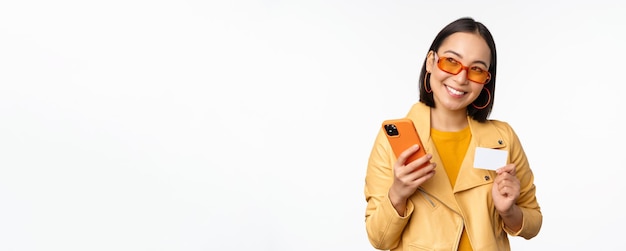 Bezpłatne zdjęcie koncepcja zakupów online i dostawy szczęśliwa koreańska dziewczyna w stylowych ubraniach posiadających kartę kredytową i sm