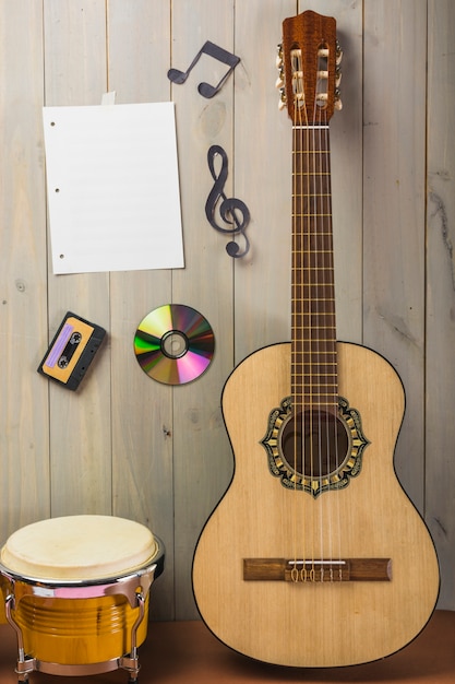 Pusta strona muzyczna; kaseta; płyta CD; i nuta utknęła na drewnianej ścianie z gitarą i bębnem bongo