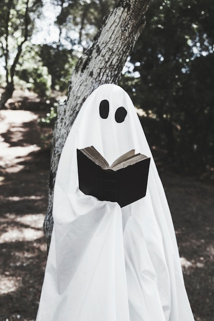 Bezpłatne zdjęcie phantom opierając się na drzewie i czytanie książki