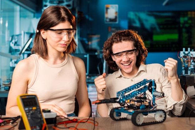 Bezpłatne zdjęcie podekscytowany młody mężczyzna i kobieta w okularach ochronnych robi eksperymenty w robotyce w laboratorium