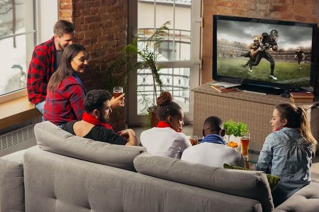 Podekscytowana grupa ludzi ogląda futbol amerykański, mecz sportowy w domu.