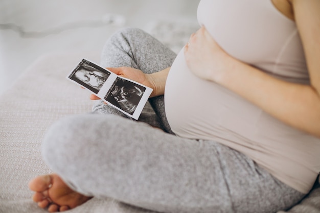 Mulher grávida com foto de ultrassom sentada na cama
