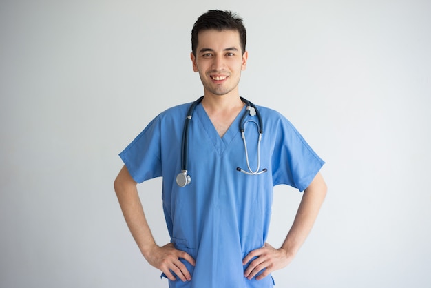 Foto grátis doutor masculino novo seguro que está e que mantém as mãos nos quadris. conceito de saúde.