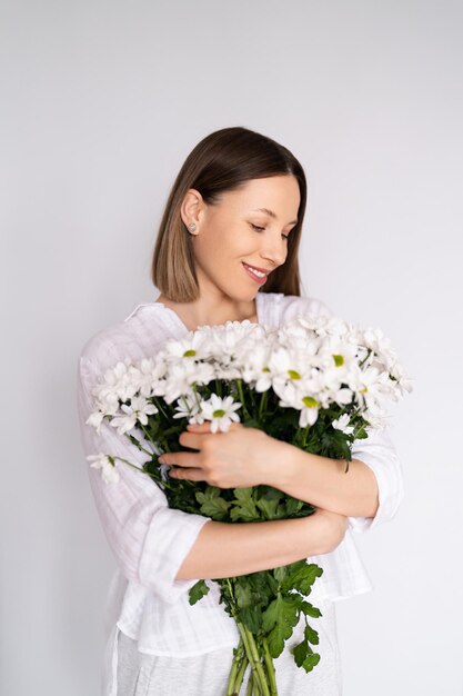 Jovem linda e linda mulher sorridente com um buquê de flores frescas brancas no fundo da parede branca