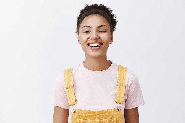 Foto grátis linda garota bonita em um macacão amarelo da moda sobre uma camiseta, sorrindo amplamente com uma expressão alegre e feliz