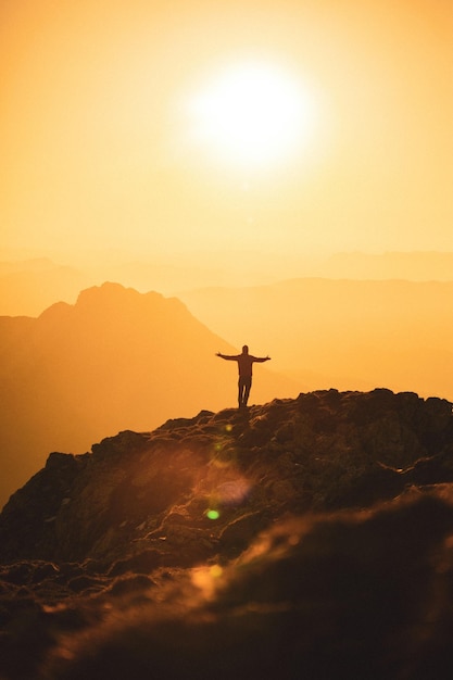 Foto grátis silhueta de um caminhante de espírito livre no topo de uma montanha ao pôr do sol dourado