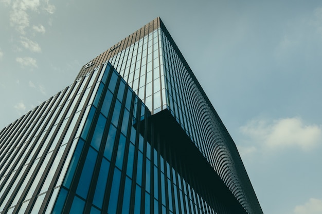 Foto grátis vista de ângulo baixo de um edifício em uma fachada de vidro sob o lindo céu nublado