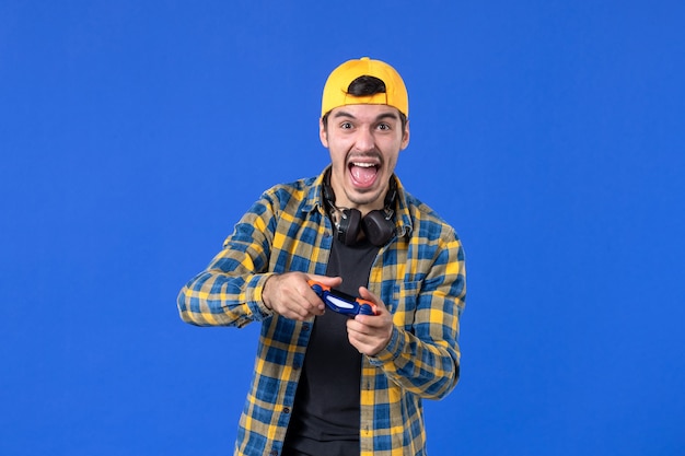 Foto grátis vista frontal do jogador masculino com gamepad jogando videogame na parede azul