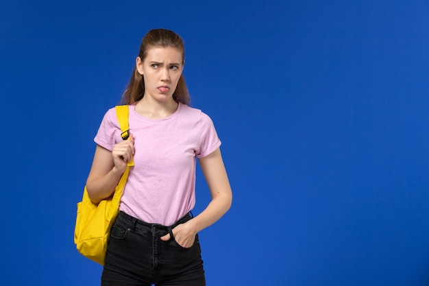 Foto grátis vista frontal de aluna em camiseta rosa com mochila amarela na parede azul