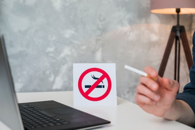 Kostenloses Foto hand des mannes, die zigarette im vorderen laptop und im nichtraucherzeichen hält