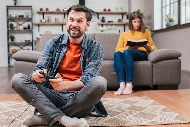 Kostenloses Foto junger mann, der das videospiel mit dem steuerknüppel und ihrer frau sitzen auf sofa am hintergrund spielt