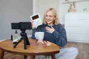 Kostenloses Foto porträt einer schönen lächelnden frau, die ein video in ihrem zimmer aufnimmt, hat eine kamera auf dem coffee-tisch