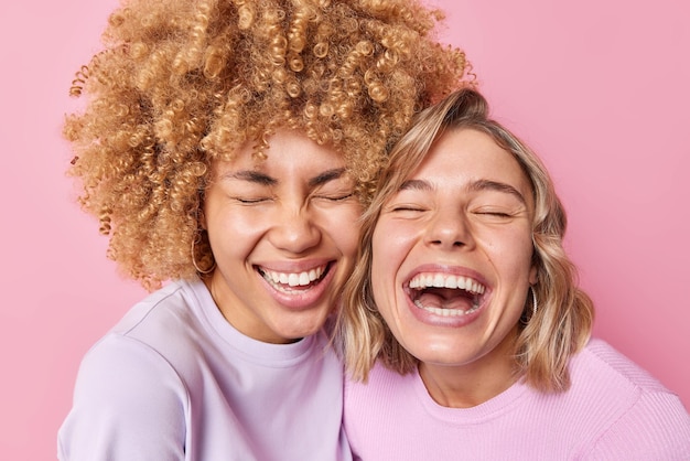 Kostenloses Foto zwei überglückliche junge frauen lachen fröhlich aus, halten die augen geschlossen, stehen eng beieinander, gekleidet in freizeitkleidung, die über rosafarbenem hintergrund isoliert ist aufrichtiges menschliches gefühls- und gefühlskonzept