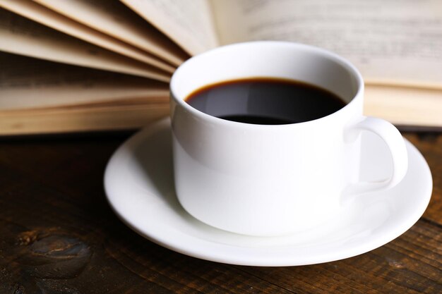 Uma chávena de café quente com um livro em fundo de madeira