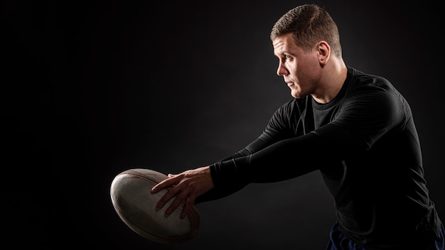 Vista lateral del jugador de rugby masculino atlético sosteniendo la bola
