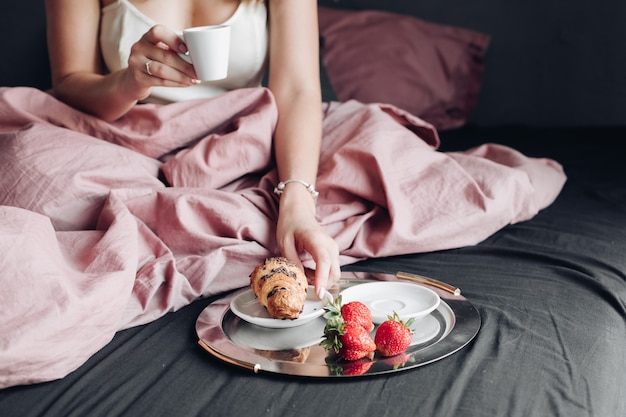 Weibliche Hände der Nahaufnahme, die das Wochenende appetitanregend frühstückend im Bett genießen