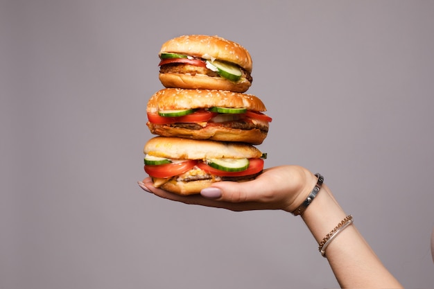Weibliche Hand, die Pyramide von dem appetitanregenden Burger drei lokalisiert an der grauen Studiohintergrundnahaufnahme hält
