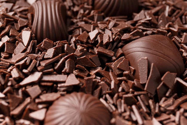Foto wunderschön geformte dunkle schokoladenbonbons, getaucht in schokoladenstückchen, nahaufnahme, konzept zur herstellung von schokoladenbonbons, schokoladenhintergrund